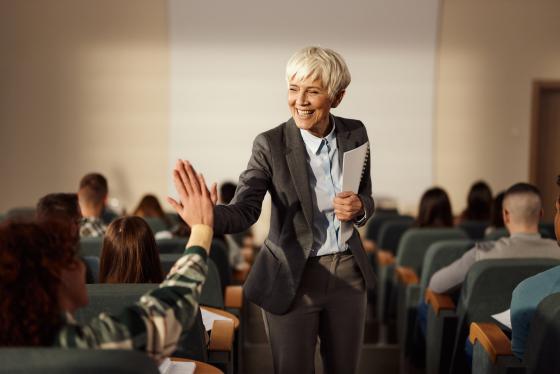 Smilende kvinnelig professor gir high-five i et auditorium