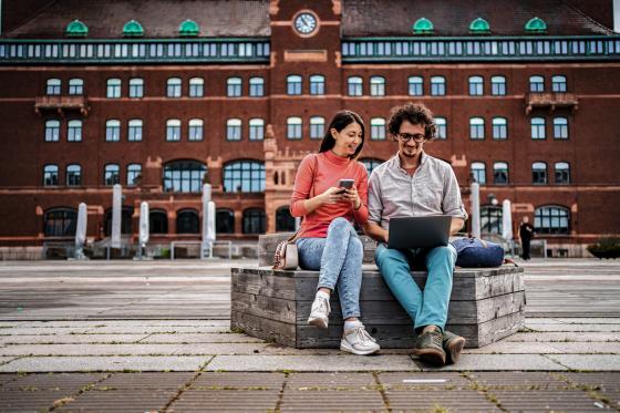 En ung kvinne og en ung mann sitter på en benk i en storby