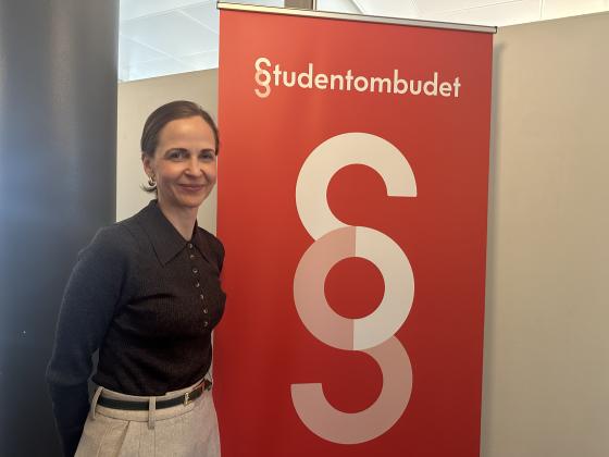 Studentombud Marianne Høva Rustberggard står foran en plakat der det står «Studentombudet»