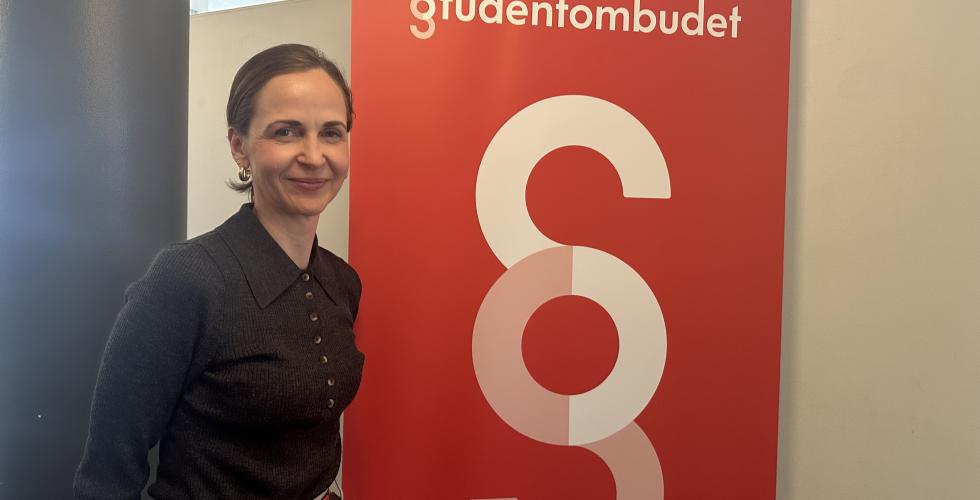 Studentombud Marianne Høva Rustberggard står foran en plakat der det står «Studentombudet»